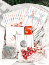 A silver star theme birthday party bash box for little kids including paper plates, cups, napkins, a crown, birthday candle, and more