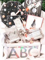 A space theme birthday party bash box for little kids including paper plates, cups, napkins, a crown, birthday candle, and more